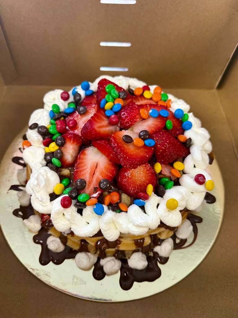 Waffle Cake topped with strawberries, M&M's, whipped cream and chocolate drizzle